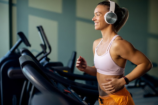 Young happy athletic woman wearing headphones while jogging on running track in health club.